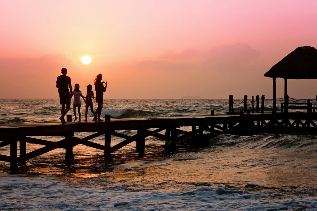 Una familia pasea por un muelle al borde del mar, al atardecer.